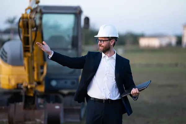 stock image Construction manager in suit and helmet at a construction site. Construction manager worker or supervisor wearing hardhat in front of house. Supervisor construction manager near excavator. Renovation