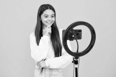 Blogging, videoblog. Teenager child blogger with phone recording video on isolated yellow studio background. Influencer teen girl speaking in front of smartphone