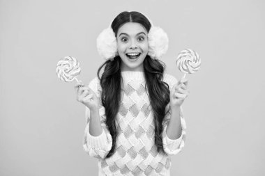 Funny child with lollipop over yellow isolated background. Sweet childhood life. Teen girl with yummy caramel lollipop, candy shop. Teenager with sweet sucker