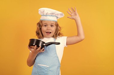 Funny kid chef cook with kitchen pot stockpot. Child wearing cooker uniform and chef hat preparing food on kitchen, studio portrait. Cooking, culinary and kids food concept