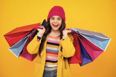 Kış alışverişi. Sarı arka planda alışveriş torbaları olan güzel moda kızı. Alışveriş ve moda alışverişi. Alışveriş çantalı çocuk. Heyecanlı genç kız