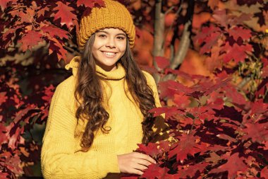 smiling teen kid in hat at autumn leaves on natural background.