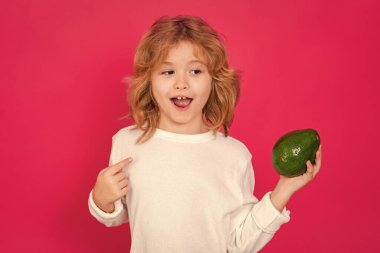 Kid hold red avocado in studio. Studio portrait of cute child with avocado isolated on red background