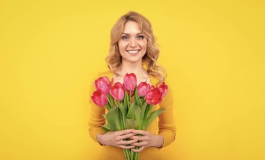 Sarı arka planda bahar lale çiçekleriyle gülümseyen genç kız..