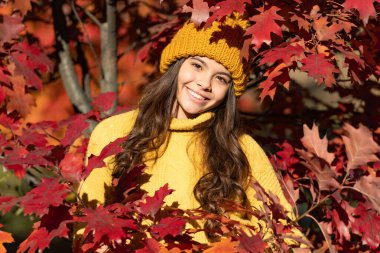 Sonbahar sonbaharı geçmişi olan genç bir kız. Sonbahar modasında çocuk portresi sıcak çocuk kıyafetleri. Sonbaharda şapkalı pozitif çocuk doğal arka planda kalıyor..