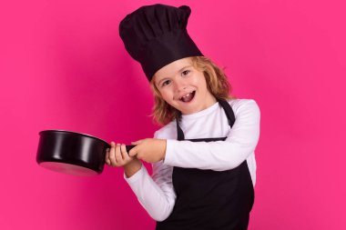 Aşçı çocuk tencereyle yemek yapıyor. Heyecanlı aşçı şefi. Çocuk fırın üniforması ve aşçı şapkası giyiyor yemek hazırlıyor, stüdyo fotoğrafı çekiyor.