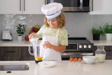 Funny kid chef cook cookery at kitchen. Chef kid boy making healthy food. Portrait of little child in chef hat