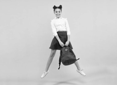Back to school. Teenager schoolgirl in school uniform with bag. School children on isolated blue studio background. Jump and run. Happy teenager, positive and smiling emotions of teen girl