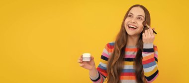 Mutlu çocuk makyaj malzemelerini toz fırçası sarı arka planda kullanıyor. Genç çocuklar için makyaj malzemeleri, poster tasarımı. Güzellik çocukları makyaj, fotokopi alanı ile pankart