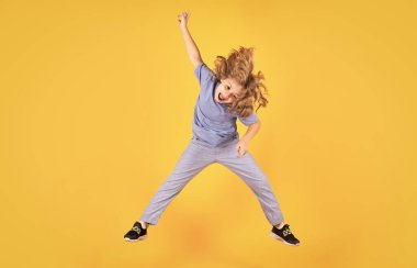 Funny boy jumping in air. Kid boy jump fly movement wear shirt and jeans isolated on yellow studio background