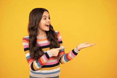 Close-up portrait of her she nice cute attractive cheerful amazed girl pointing aside on copy space isolated on yellow background. Happy teenager, positive and smiling emotions of teen girl