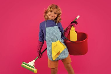 Portrait of funny child cleaning. Housekeeping and home cleaning concept. Child use duster and gloves for cleaning. Studio isolated pink background