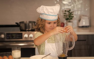 Fun kids kitchen. Funny little kid chef cook wearing uniform cook cap and apron cooked food in the kitchen. Kids are preparing food, bake cookies in the kitchen