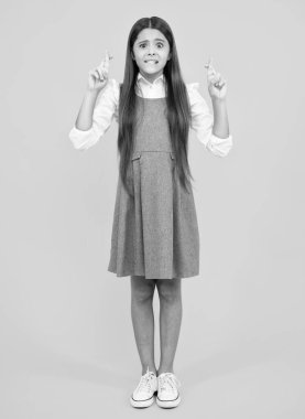 Portrait of adorable little teenager gitl standing with biting lips and crossing fingers, wishing for good luck. Childhood dreams and hopes