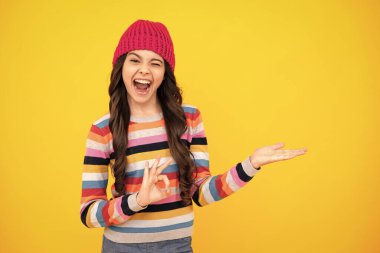 Amazed teenager. Teenager girl with winter hat over isolated yellow background. Winter christmas holidays, new year mood. Kids warm clothes. Excited teen girl