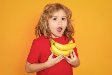 Child in red t-shirt hold banana in studio. Studio portrait of cute kid boy with bananas isolated on yellow background, copy space