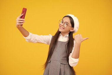 Çocukların selfie 'si. Cep telefonu tutan mutlu ve gülümseyen ergen çocuk. Güzel bir genç kızın cep telefonu, cep telefonu uygulaması kullanarak yakın plan portresi, parlak sarı arka planda izole edilmiş.