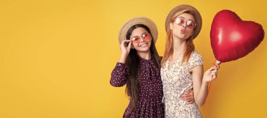 Mother and daughter kid banner, copy space, isolated background. happy mom and daughter hold love heart balloon on yellow background