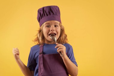 Funny kid chef cook with spoon, studio portrait. Cooking children. Chef kid boy making healthy food. Portrait of little child in chef hat isolated on studio background. Kid chef. Cooking process