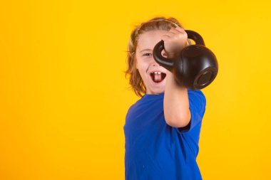 Çocuklarla boş zamanlarında spor aktiviteleri. Kettlebell tutan sarışın çocuk. Çocuklar için spor egzersizleri. Halterleri kaldıran komik çocuk.