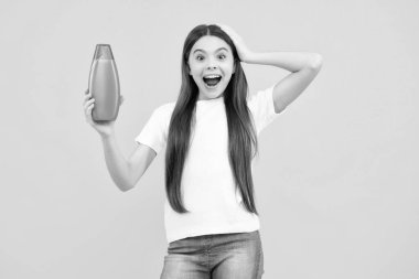 Şampuan kremi kullanan bir çocuk. Günlük kozmetik bakım. 12, 13, 14 yaşlarındaki ergen çocuğun elinde saç ve cilt bakımı şişesi var. Güzellik sağlığı ve kozmetik ürünleri. Heyecanlı bir genç, şaşkın duygular içinde