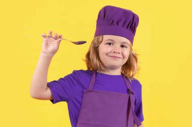 Komik çocuk aşçı kaşıkla aşçı, stüdyo portresi. Aşçı çocuk, stüdyo resmi. Çocuklar yemek yapıyor. Önlüklü ve aşçı şapkalı çocuk.