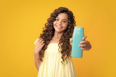 Mutlu ergen portresi. Sarı arka planda şampuan şişesi ya da duş jeli olan genç bir kız çocuğu. Çocukların saçı kozmetik üründür. Gülümseyen kız