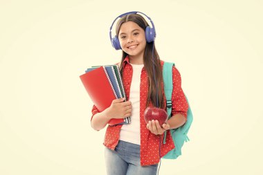 School girl, teenage 12, 13, 14 years old in headphones and books on isolated studio background. School kids with backpack. Portrait of happy smiling teenage child girl