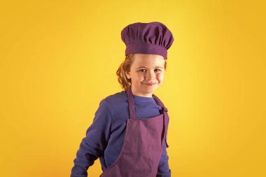 Aşçı çocuk sağlıklı yemek yapıyor. Stüdyo arka planında izole edilmiş, şef şapkalı küçük çocuk portresi. Çocuk aşçı. Yemek pişirme süreci