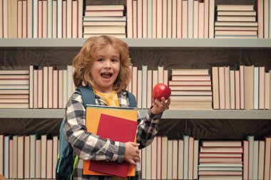 School boy with books and apple in library. School child 7-8 years old with book go back to school. Little student