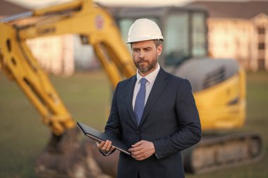 Kazıcının yanında inşaat işçisi. Evin önünde kendine güvenen bir inşaat sahibi. Mimar, inşaat mühendisi. İnşaat alanında güvenlik yeleği ve kasketi olan bir inşaat sahibi.