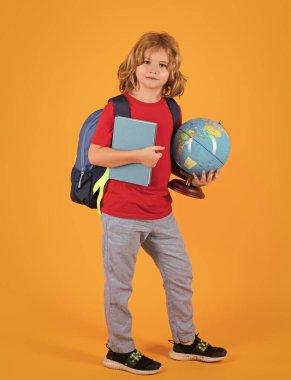 Kid from elementary school. School child boy in school uniform with bagpack book and apple. School children on studio isolated yellow background