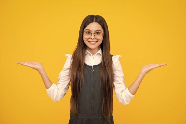 Onun yakın plan portresi. Güzel, çekici, neşeli, şaşkın kız, sarı arka planda izole edilmiş fotokopi alanını işaret ediyor. Mutlu kız yüzü, pozitif ve gülümseyen duygular