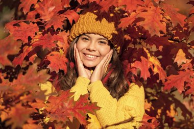 Sonbahar arka planında bir kız çocuğu, sonbahar çocuklarının yüzü. Sonbaharda şapkalı neşeli kız doğal arka planda yapraklar bırakıyor..