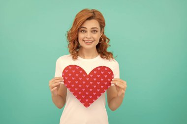 Mutlu kızıl saçlı kadın, kırmızı kalbi mavi arka planda tut.