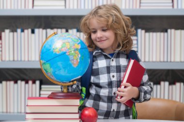 School boy looking at globe in library, geography lesson. School child student learning in class, study english language at school. Elementary school child. Portrait of funny pupil learning