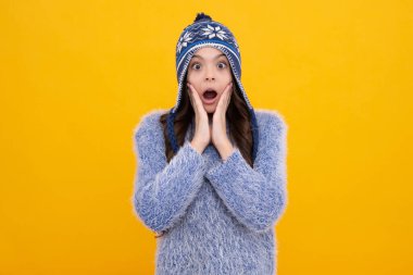 Moda tutkunu, örgü şapkalı ve kazaklı genç bir kadın renkli mavi arka planda eğleniyor. Şaşırmış genç kız.