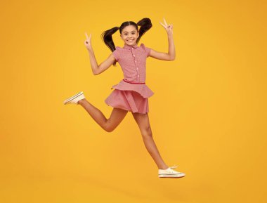 Excited face. Amazed expression, cheerful and glad. Full length little overjoyed teen girl 12, 13, 14 year old jump and run isolated on yellow background studio