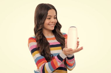 Şampuan kremi kullanan bir çocuk. Günlük kozmetik bakım. Gençlerin elinde saç ve cilt bakımı şişesi var. Güzellik sağlığı ve kozmetik ürünleri. Mutlu kız yüzü, pozitif ve gülümseyen duygular