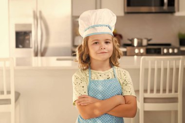 Mutfaktaki komik çocuk şefin portresi. Aşçı aşçı çocuk mutfakta yemek hazırlıyor. Çocuk lezzetli yapıyor. Yemek pişirme