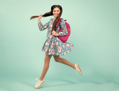 Okul üniformalı okul çantalı kız. Liseli gençler sırt çantalarını mavi izole arka planda tutarlar. Koş ve atla. Mutlu ergen, pozitif ve gülümseyen duygular