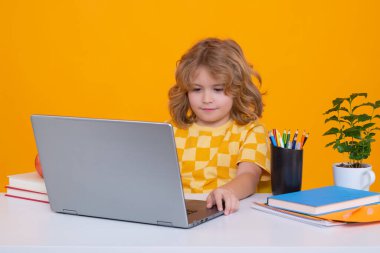 Dizüstü bilgisayar kullanan tatlı bir okul çocuğu. Okul ve eğitim kavramı. Sarı arka planda izole edilmiş şirin çocuk portresi. Okula geri dön.