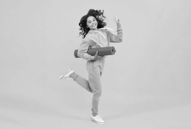 Girl teenager in tracksuit. Run and jump. Happy cute child in a yellow sports suit on a yellow background. Sportswear advertising concept