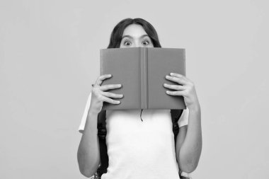 Okul çantalı genç kız sarı izole edilmiş stüdyo geçmişi üzerine kitap tutuyor. Çocuk okulu ve eğitim konsepti