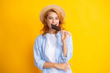 Neşeli, komik genç kızın portresi soğuk dondurulmuş tatlı yemekten, lezzetli çikolatalı dondurma yemekten, sarı arka plandan hoşlanıyor.