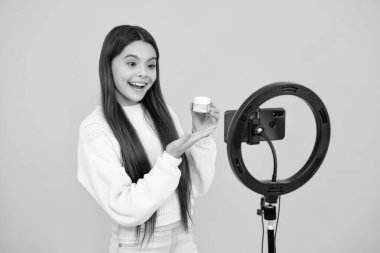 Teen girl blogger influencer use selfie led lamp and smartphone on tripod for making online video tutorial. Lifestyle kids blog. Beauty blog, presenting makeup cosmetics powder and brush
