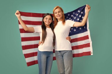 Vatansever bayram. Mutlu aile, mavi izole edilmiş stüdyo geçmişinde Amerikan bayrağı taşıyan anne ve kızı. ABD 4 Temmuz 'da bağımsızlığını kutladı
