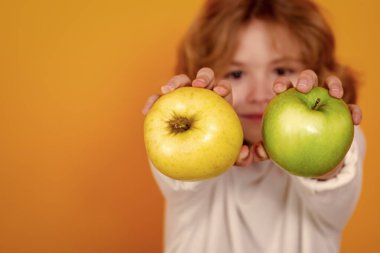Close up kid with apple in studio, selective focus. Studio portrait of cute child hold apple isolated on yellow background