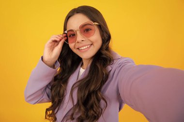 Trendy beautiful teenage model making selfie posing on yellow studio background. Teen fashion