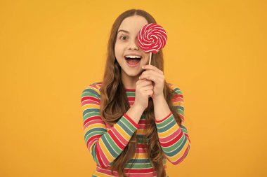 Cool teen child with lollipop over yellow isolated background. Sweet childhood life. Teen girl with yummy lollipop candy. Excited face, cheerful emotions of teenager girl